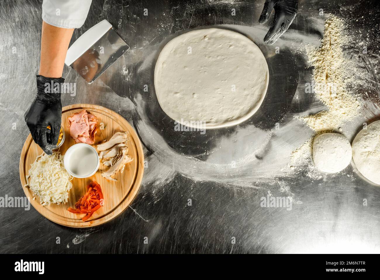 Cooking pizza on a steel table; dough, flour, pizza topping, sauce and chef`s hands in black gloves on the table Stock Photo